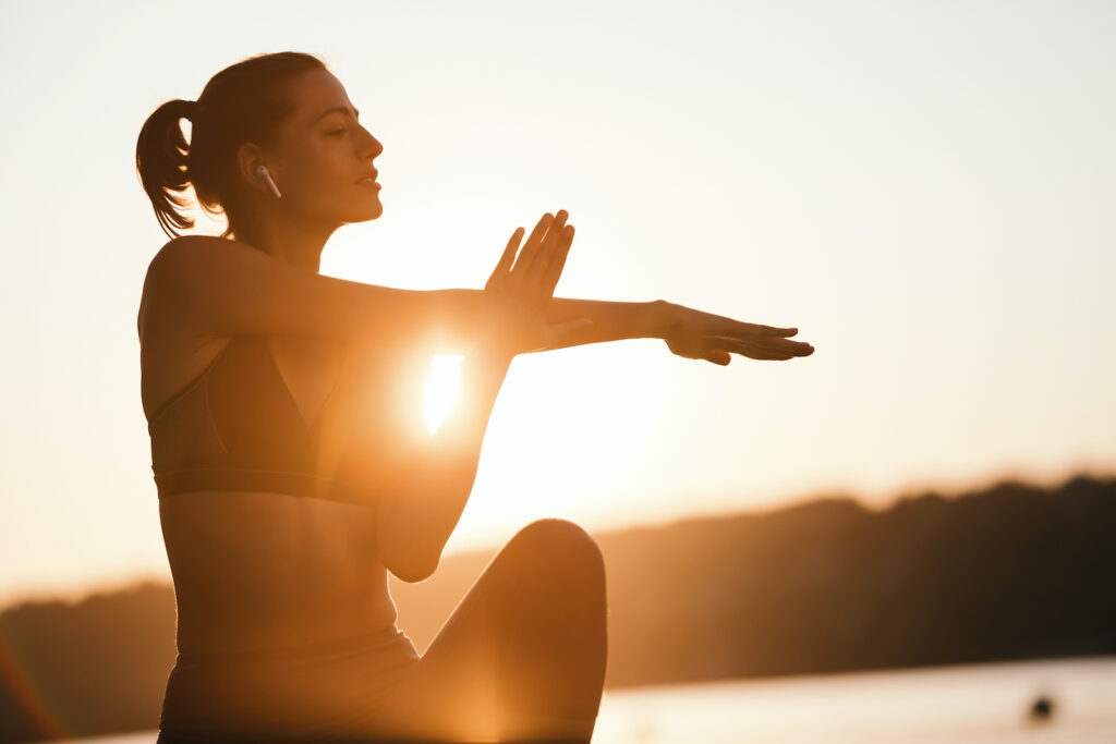 Female athlete stretching her arms at sunset in nature